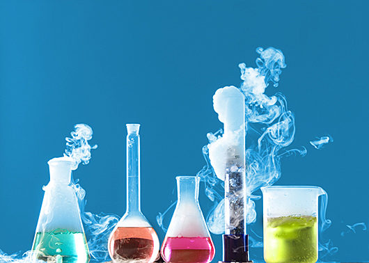 lab beakers and flasks filled with colourful liquid giving off fumes